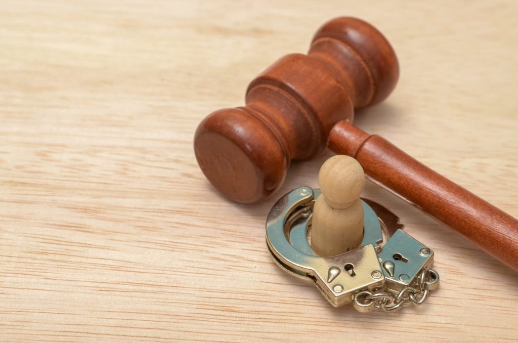 The handcuffs are clasped around the wooden figure, symbolizing imprisonment or legal restraint.