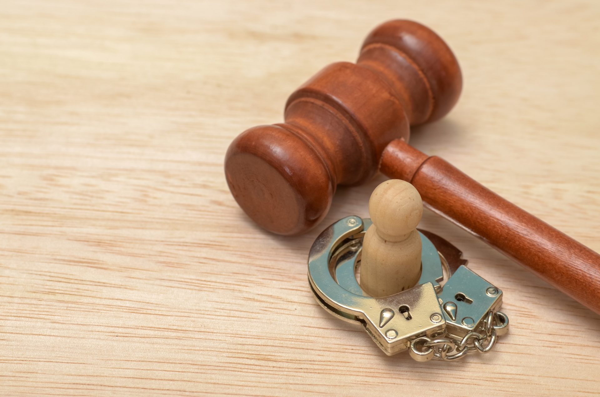 The handcuffs are clasped around the wooden figure, symbolizing imprisonment or legal restraint.